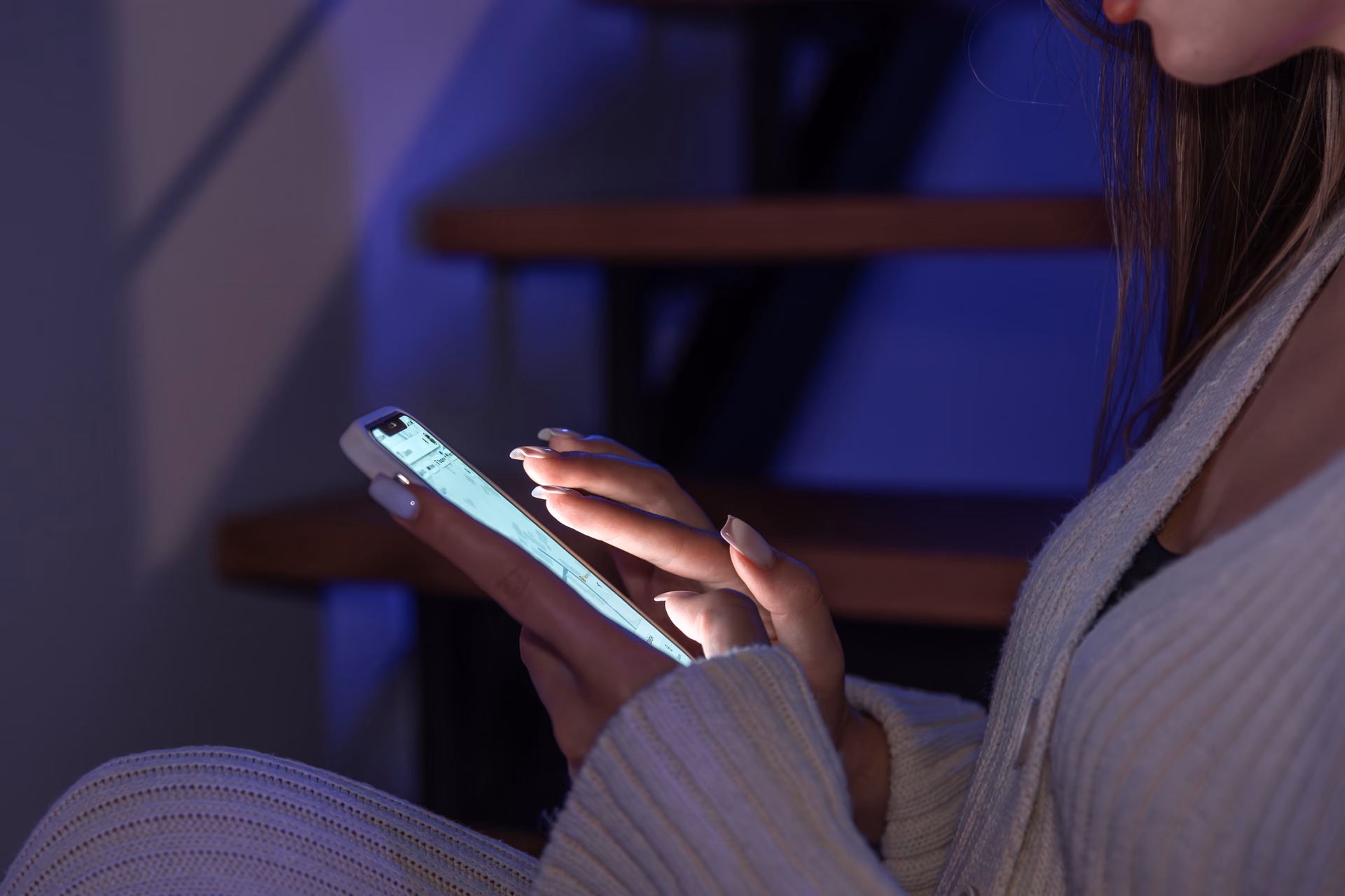 Woman scrolling her phone feed at night, screen glowing blue against a dark background, illustrating the question how much does social media marketing cost.